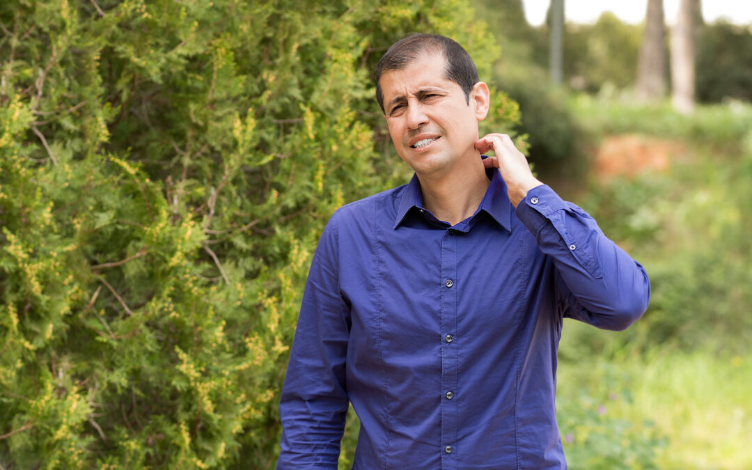 Man suffering itching scratching neck standing outdoors in a park